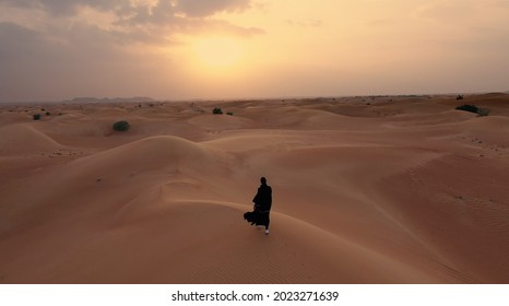 AERIAL. Camera following woman in traditional Emirati dress walking in a desert in strog wind and sunset. - Powered by Shutterstock