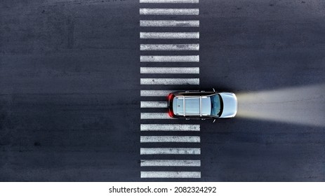 Aerial. A car with its headlights on drives over a pedestrian crosswalk at night. Top view from drone. - Shutterstock ID 2082324292