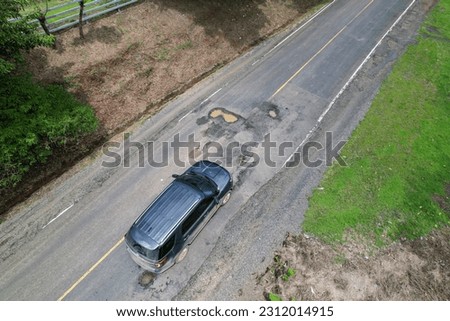 AERIAL: Careful car drive among big potholes on an asphalt road in tropics. Road challenges for a car travelling through tropical countryside. Damaged roadways and poor road maintenance in third world