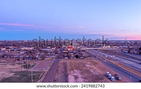 Aerial Cityscape of Lubbock Texas with traffic on the roads and tall buildings in the background against a blue sky at sunrise.