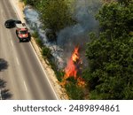 Aerial close up view from drone A fire truck has just arrived to put out the fire. European road with burning bushes due and smoke to a thrown cigarette butt