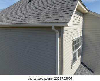 Aerial closeup view gable with vinyl siding, white frame gutter guard system, fascia, drip edge, soffit, on a pitched roof attic at a luxury American single family home neighborhood USA