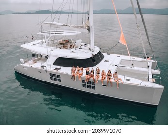 Aerial Copter's Picture With Young Handsome Women In Swimsuits  Sunglasses Posing Sitting On A Expensive White Yacht In The Open Big Sea. The Background Is The Coast. The Concept Of A Photo Session.