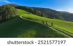 AERIAL: Cycling friends enjoying a serene ride along a green hilltop bike trail bathed in gentle morning light with stunning views of rolling hills and nature. Mountain biking on a sunny autumn day.