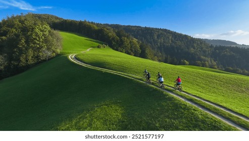 AERIAL: Cycling friends enjoying a serene ride along a green hilltop bike trail bathed in gentle morning light with stunning views of rolling hills and nature. Mountain biking on a sunny autumn day. - Powered by Shutterstock