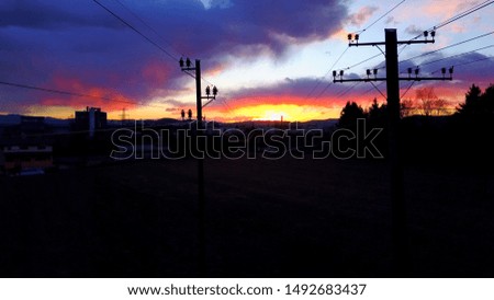 AERIAL Dramatic colorful sunset in small industrial town surrounded by rocky mountains. Houses, blocks, flats & apartments in suburban town at gorgeous red, orange and pink sunrise. Electrical pylons