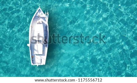 Aerial drone bird's eye top view of white traditional fishing boat in turquoise clear waters, Cyclades, Greece