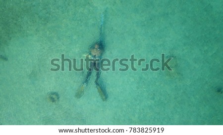 Aerial drone bird's eye view photo of submerged spearfishing diver in tropical turquoise clear water rocky seascape