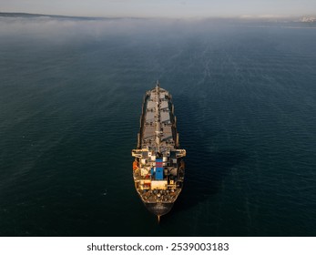 Aerial drone footage of a cargo ship sailing on misty waters with sunlight reflections, creating a calm and mysterious maritime scene, perfect for industrial and nautical themes - Powered by Shutterstock