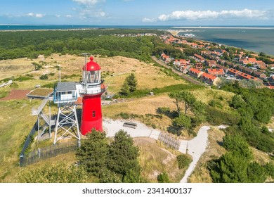 Aerial drone image of the island Vlieland. With bright red lighthouse on top of a sand dune overlooking the small town, Terschelling, the North Sea and the Wadden Sea. Blue sky, summer and red roofs