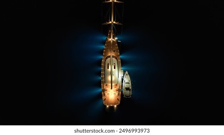 Aerial drone night shot of beautiful illuminated luxury sail boat with wooden deck anchored in deep blue Mediterranean sea - Powered by Shutterstock