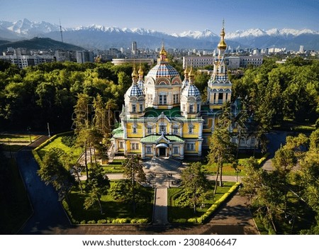 Aerial drone panorama of the Ascension Cathedral Russian Orthodox church and snow mountains at background in Panfilov Park against blue sky in Almaty city, Kazakhstan