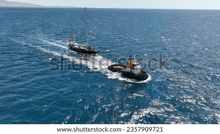 Aerial drone photo of assistive tug boat towing small sail boat to shipyard in deep blue sea