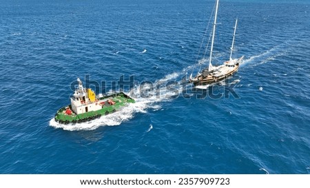 Aerial drone photo of assistive tug boat towing small sail boat to shipyard in deep blue sea