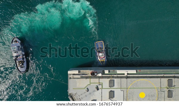 Aerial drone photo of large\
car carrier ro ro vessel guided by tug boats to dock to\
Mediterranean port