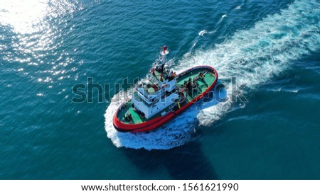 Aerial drone photo of tug boat cruising in high speed near cruise liner docked in Mediterranean port