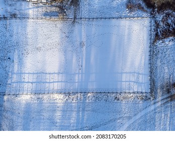 Aerial, drone photography of a empty paddock covered in snow. Winter season in Sweden. Bird's eye view of enclosed pasture. Texture of shadows, traces of horses and footprints on the ground. 
