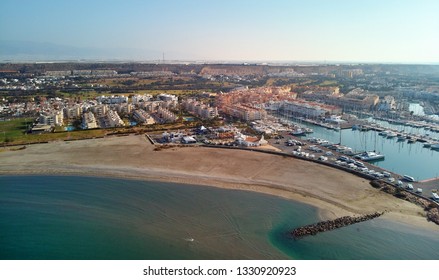 Aerial drone point view photography Almerimar townscape, empty beach sandy coastline, nautical vessels moored in the harbor marina resort, green water sea bay, blue clear sky sunny day, Almeria, Spain