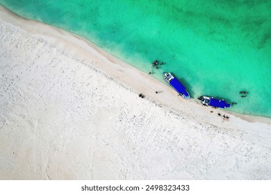 Aerial drone shot of boats on beach with sand. Two blue boats. Shallow water. Diagonal. White Sand. People on the beach. - Powered by Shutterstock