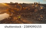 Aerial Drone Shot Of Construction Site On Sunny Evening: Industrial Excavators Digging Rocks And Loading Them Into A Truck. Engineer And Architect Observing Process, Discussing Real Estate Project