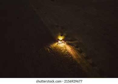 An Aerial Drone Shot Of A Harvester Machine Working On A Field With Lights On At Night