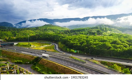 Aerial Drone Shot: Long Haul Semi Trucks Driving on the Busy Highway in the Rural Region of Italy. Beautiful Mountains with Forest and Clouds in the Background