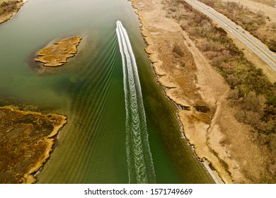 Aerial Drone Shot Over A Boat Speeding By, Leaving Behind A Beautiful Wake Pattern, As It Sails Through The Waters In The Salt Marsh On A Chilly Fall Day, Taken In Freeport, New York