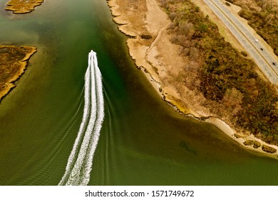 Aerial Drone Shot Over A Boat Speeding By, Leaving Behind A Beautiful Wake Pattern, As It Sails Through The Waters In The Salt Marsh On A Chilly Fall Day, Taken In Freeport, New York