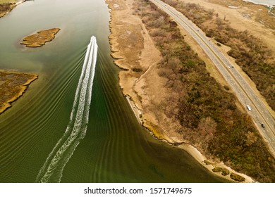 Aerial Drone Shot Over A Boat Speeding By, Leaving Behind A Beautiful Wake Pattern, As It Sails Through The Waters In The Salt Marsh On A Chilly Fall Day, Taken In Freeport, New York