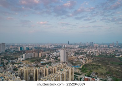 Aerial Drone Shot Passing Over A Building With Homes, Offices, Shopping Centers Moving Towards Skyscapers In Front Of Sunset Showing The Empty Outskirts Of The City Of Gurgaon India Asia