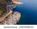 Aerial drone shot of a rocky coastline and coastal road near the sea with cars