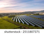 Aerial drone shot of rows of solar panels in lush fields showcase green energy innovation, harmonizing with nature for sustainable electricity under sky.