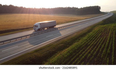 Aerial Drone Shot: Semi Truck With Cargo Drives Along A Wide Highway Through A Scenic Valley In The Sun At Dawn. Concept Of Logistics, Transport, Cargo Transportation, Delivery.	
