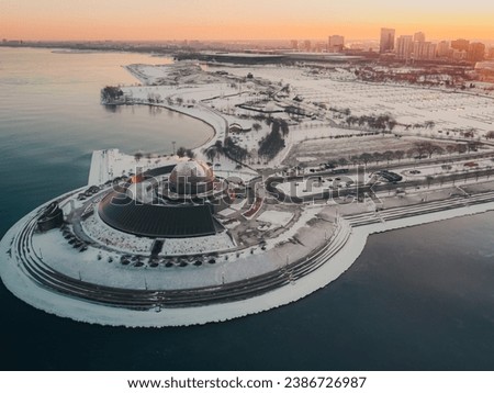 An aerial drone snow view of Adler Planetarium on a cold winter day on a museum campus in Chicago, Illinois, United States. Landscape view with lake, road, trees, and buildings. 