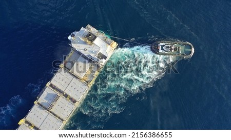 Aerial drone top down photo of tow - tug boat assisting by pulling empty container ship to depart from container terminal port