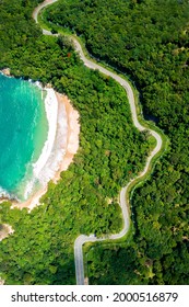 Aerial drone top down view of waves breaking in the sand with road and forest. High angle view of tropical sea with Seafront road.