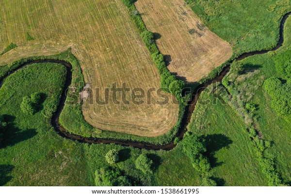 Aerial drone top down\
view on european green meadows, wheat fields and forest divided by\
snake like river