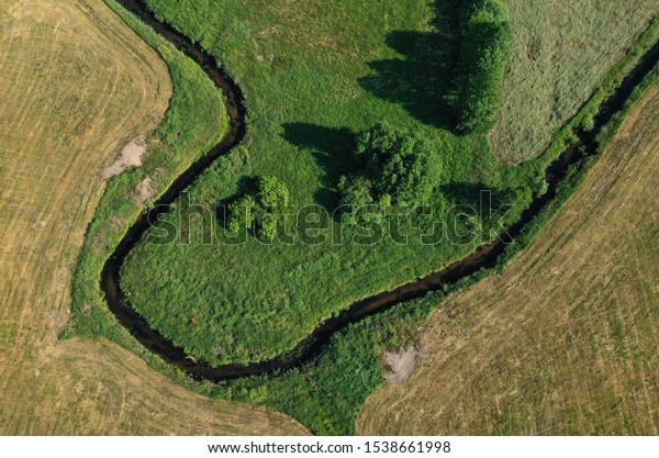 Aerial drone top down\
view on european green meadows, wheat fields and forest divided by\
snake like river