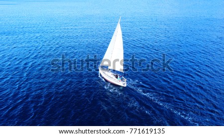 Aerial drone top view photo of sail boat with white sails, sailing in Mediterranean Aegean island of Santorini, Cyclades, Greece