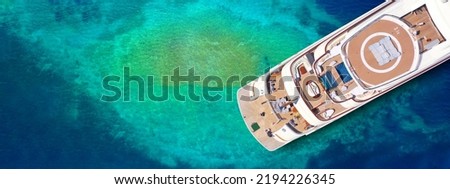 Aerial drone top view ultra wide photo of large luxury yacht - boat stern with helicopter landing area anchored in tropical exotic paradise with turquoise sea