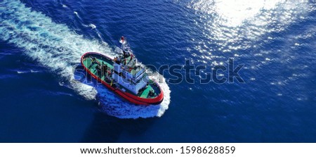 Aerial drone ultra wide photo of industrial tug assisting boat cruising in deep blue Mediterranean sea