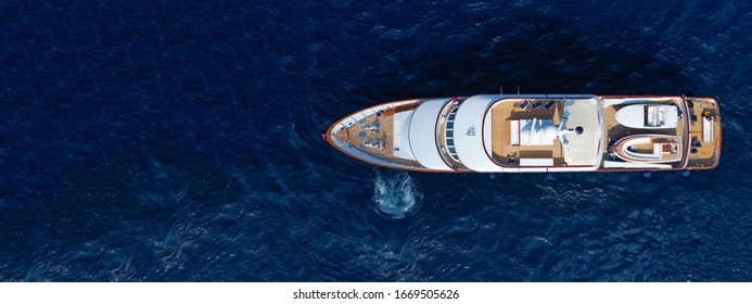 Aerial drone ultra wide top down photo of luxury yacht with wooden deck anchored in deep blue sea of Mykonos island, Cyclades, Greece