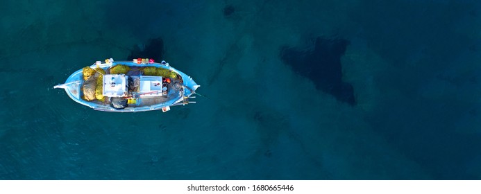 Aerial drone ultra wide top down photo of traditional wooden fishing boat near crystal clear sea of old port of Mykonos island, Cyclades, Greece
