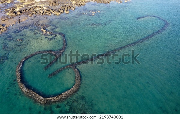 Aerial drone view above the One-Heart Stacked Stones,\
which is a traditional fishing weir (a Fish Trap) and a popular\
tourist attraction, in Xiyu, Penghu County, Taiwan, on a sunny\
summer day