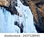 Aerial drone view of athlete in orange jacket Ice climbing at big frozen waterfall in Barskoon gorge the mountain valley in Kyrgyzstan