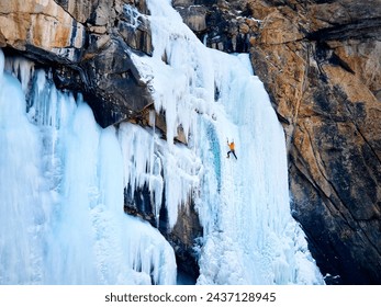 Aerial drone view of athlete in orange jacket Ice climbing at big frozen waterfall in Barskoon gorge the mountain valley in Kyrgyzstan - Powered by Shutterstock