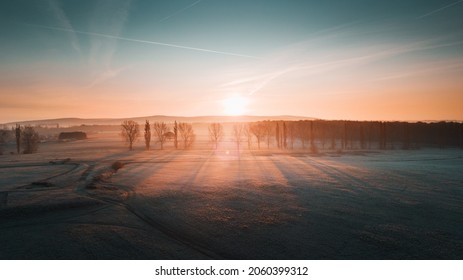 Aerial Drone View Of A Beautiful Morning Frozen Landscape With Warm Bright Light Glow Of The First Sun. Early Morning Winter Nature With Foggy Landscape And Orange Sunlight. Calm And Peaceful Frozen