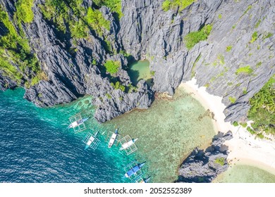 Aerial drone view of boats over a tropical coral reef and remote sandy Hidden Beach, El Nido, Palawan, Philippines.