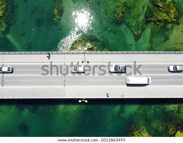 Aerial drone view\
of bridge above beautiful green river. Cars and pedestrians moving\
on bridge, view from above. Transportation. Modern concrete bridge\
over the lake.