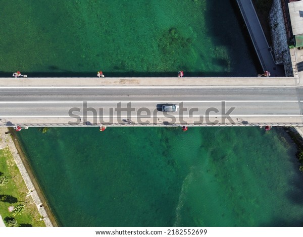 Aerial drone view\
of bridge above beautiful green river. Cars and pedestrians moving\
on bridge, view from above. Transportation. Modern concrete bridge\
over the water.